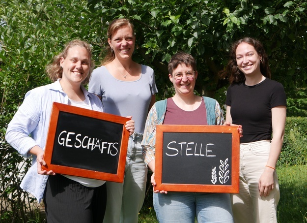Foto des Teams der Geschftsstelle. 4 Personen mit Schild